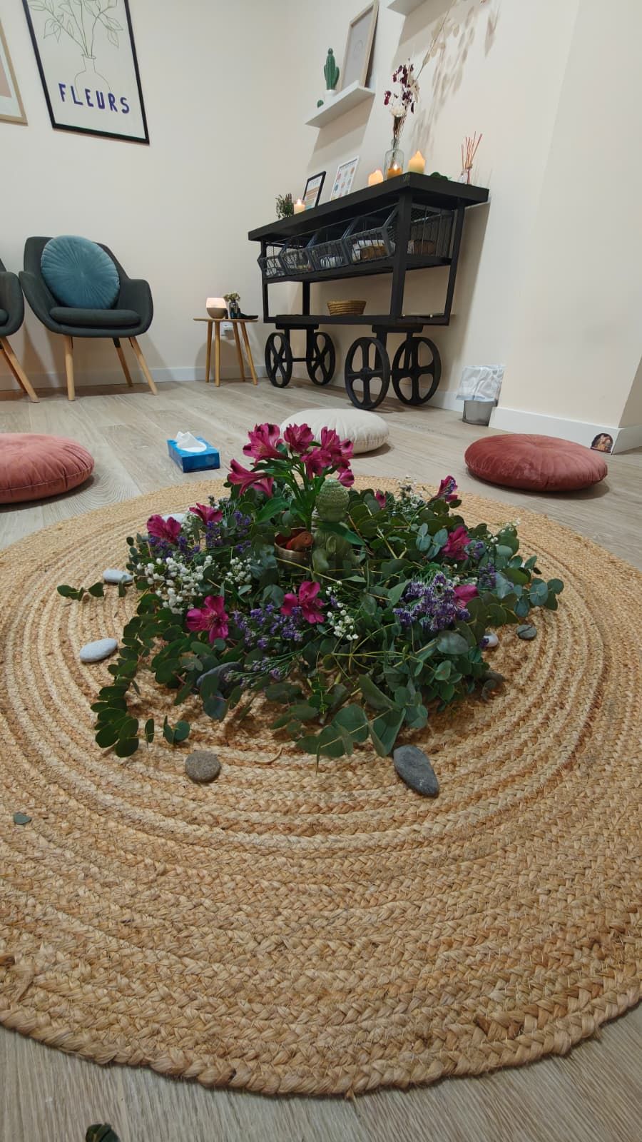 Centro de flores y piedras sobre una alfombra redonda de yute, con cojines de suelo alrededor