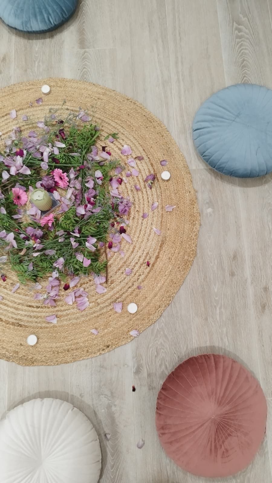 Pétalos, flores y velas sobre una alfombra de yute, rodeados de cojines de suelo